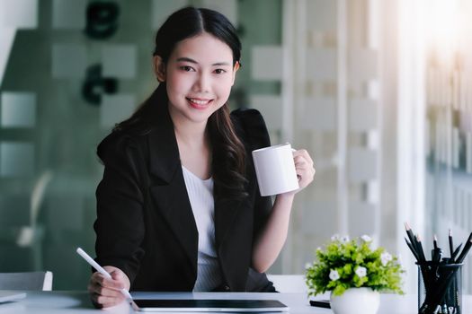 Female marketing managers drink coffee while working to reduce drowsiness before using tablet computer, and marketing analysis papers