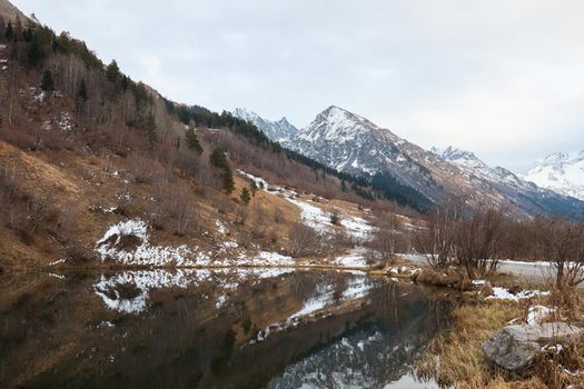 autumn landscape, lake in the mountains, water surface, fallen trees, coniferous forest and the first snow, mountains on the background