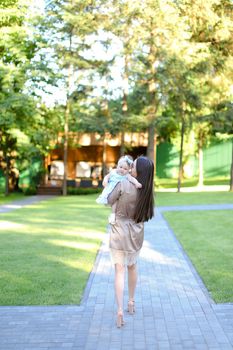 Back view of brunette mother holding little daughter in park. Concept of motherhood and resting on open air.