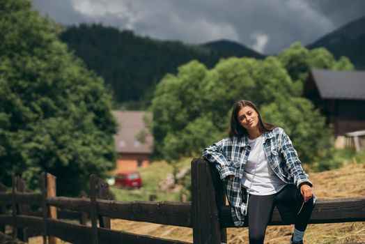 A young attractive Caucasian female sitting on a fence and posing at camera