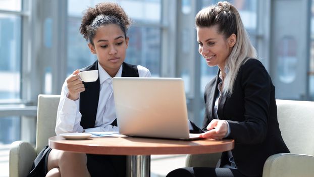 Two business women in modern office building cafe working with laptop