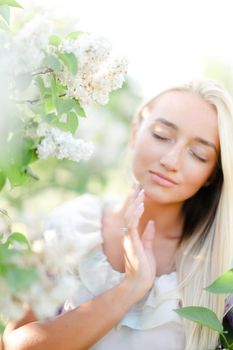 Closeup face of blonde woman with closed eyes and white lilac flowers.