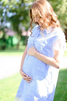 Happy pregnant girl wearing blue dress holding belly. Concept of expectant female person and motherhood.