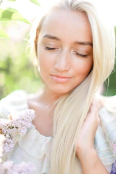 Closeup face of blonde girl with closed eyes and white lilac flowers. Concept of spring inspiration and human beauty.