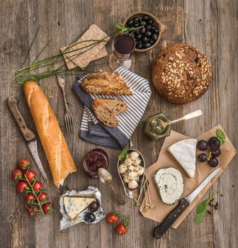 Cheese, wine and other food ingredients on a wooden table. French snacks on a wooden background.