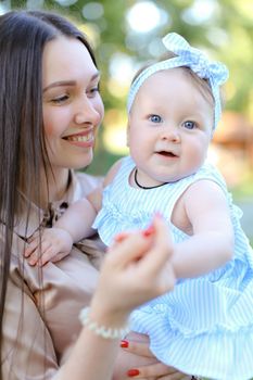 Closeup young smiling mother holding little female child in blue dress. Concept of motherhood and child.