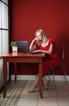 Young adult woman sitting at the table and working on laptop