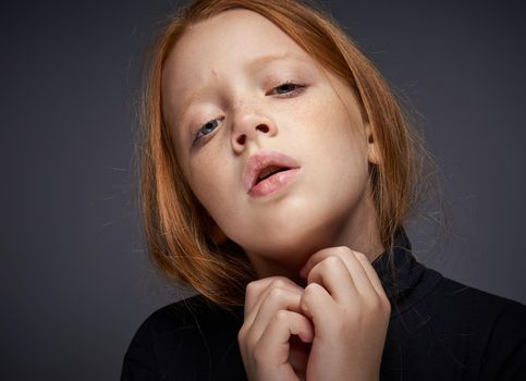 red-haired girl with freckles on her face in a black sweater posing. High quality photo