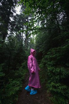 woman in raincoat walking by rainy forest