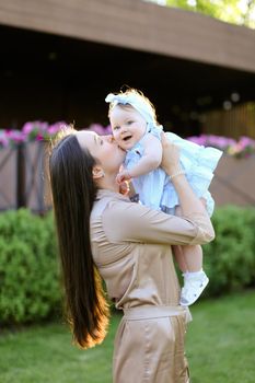 Young brunette mother holding and kissing little daughter in grass background. Concept of motherhood and child.