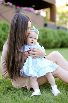 Young woman with long hair sitting on grass with little female baby. Concept of motherhood and children, resting on open air.