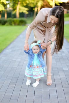 Young mother walking with little daughter in park. Concept of female child and motherhood.