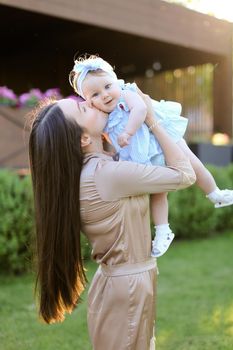 Young mother with long hair holding and kissing little daughter in grass background. Concept of motherhood and child.