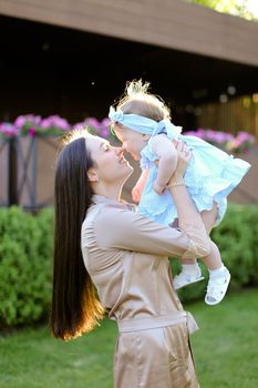 Young mother holding and kissing little daughter in grass background. Concept of motherhood and child.