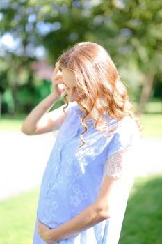 Happy young pregnant girl wearing blue dress holding belly. Concept of expectant female person and motherhood.