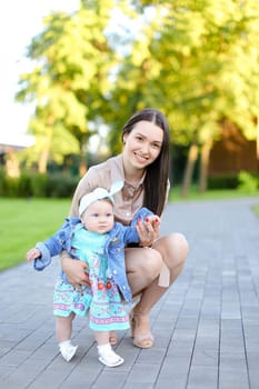 Young brunette mother walking with little daughter in park. Concept of female child and motherhood.