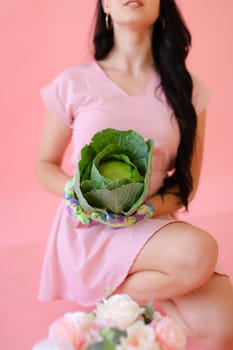 Young brunette girl keeping cabbage on pink wall background. Concept of harvest photo session at studio.