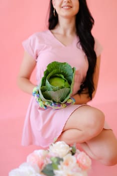 Young brunette smiling girl keeping cabbage on pink wall background. Concept of harvest photo session at studio.