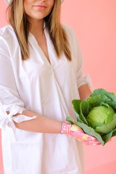 Young woman keeping cabbage in pink monophonic background. Concept of harvest photo session at studio.