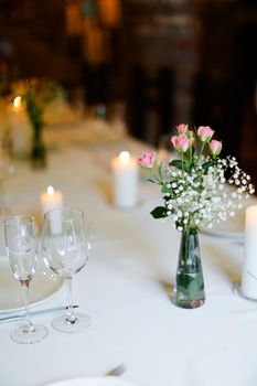 Bouguet of flowers, plates and white candles on table. oncept of romantic dinner and catering establishment.