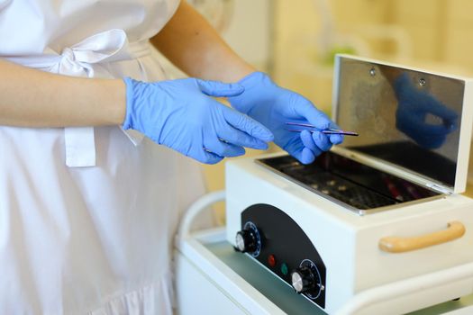 Close up cosmetologist hands in blue latex gloves disinfecting microblading pen tool at beauty salon. Concept of permanet makeup artist and cosmetology equipment.