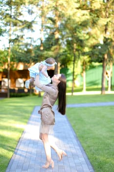 Young caucasian mother wearing dress holding little baby in garden. Concept of motherhood and resting on open air in park.