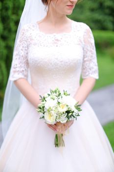 aucasian young bride keeping bouquet of flowers and wearing white dress with veil. Concept of wedding photo session.