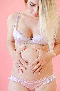 Caucasian pregnant woman wearing underwear and holding belly in pink monophonic background. Concept of expectant photo session at studio.