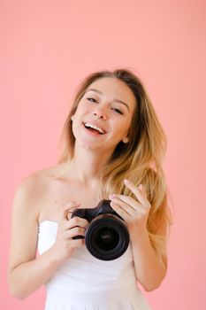 Closeup jocund gladden female photographer with black camera in pink monophonic background. Concept of modern profession and photo session.