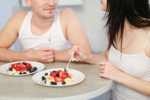 Man and woman having breakfast in kitchen, two plates with porridge and berries. Concept of happy family and eating couple.