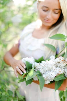 Young blonde girl keeping white lilac flowers. Concept of spring inspiration.