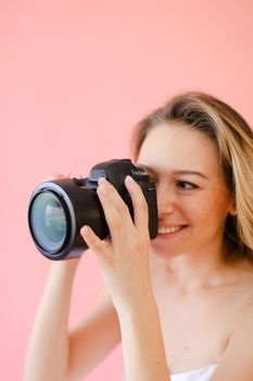 Closeup young gladden female photographer with black camera in pink monophonic background. Concept of modern profession and photo session.