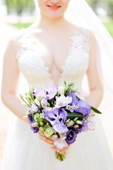 aucasian happy young bride keeping bouquet of flowers and wearing white dress with veil. Concept of wedding photo session.