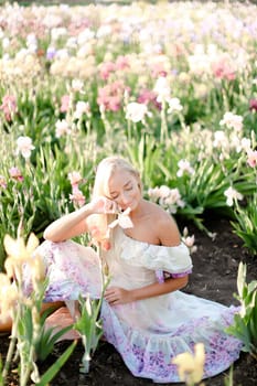 Young woman sitting near irises on garden, wearing white dress. Concept of heman beauty and spring inspiration.