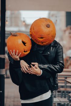 A guy and a girl with a pumpkin heads posing on the street . Halloween Concept