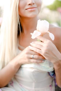 Blonde girl keeping irise flower and smiling. Concept of human beauty and flora, spring inspiration.