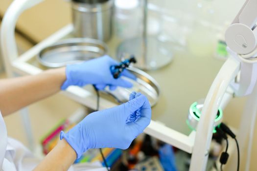 Closeup cosmetologist hands in blue latex gloves inserting needle into microblading machine at beauty salon. Concept of cosmetology equipment for permanent makeup.