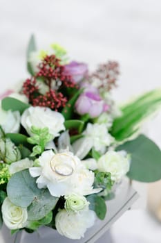 Closeup wedding cute bouquet with rings, white wall background. Concept of floristic art and bridal thigs.