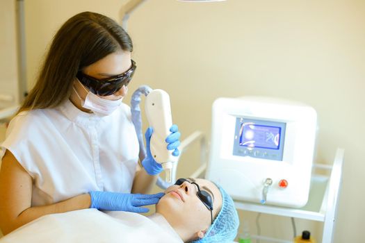 Skilled cosmetologist removing permanent makeup with laser for young girl at beauty salon. Concept of cosmetology equipment, special procedure before microblading.