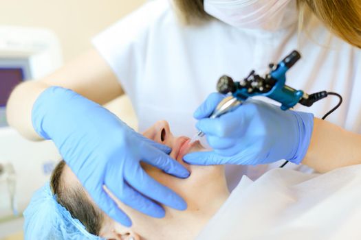 Close up hands in blue latex gloves making lip tattoo with microblading device. Concept of beauty salon, permanent makeup and cosmetology equipment.