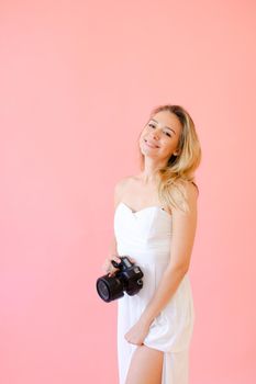 Young smiling nice female photographer with camera in pink monophonic background. Concept of modern profession and photo session.