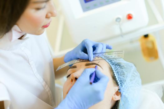 Cosmetologist shaping eyebrows before microblading. Concept of permanent makeup artist and beauty salon.