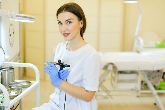 Young cosmetlogist standing with microblading machine at beauty salon. Concept of permanent makeup artist and cosmetology equipment.