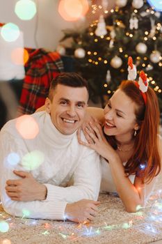 a happy married couple is lying on the floor near the Christmas tree at home.