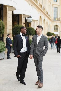 Afro american and caucasian stylish gays walking outside in city. Concept of same sex male couple.