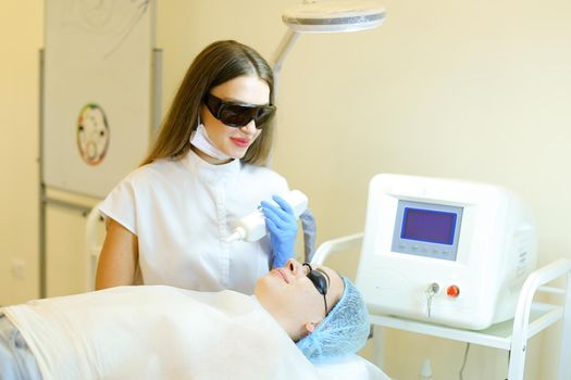 Skilled young cosmetologist removing permanent makeup with laser for young girl at beauty salon. Concept of cosmetology equipment, special procedure before microblading.