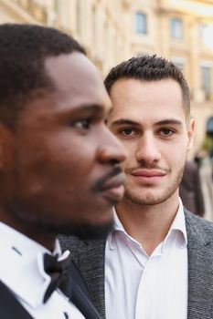 close up portrait of same sex couple. caucasian man wearing suit standing near afro american boy. Concept of business and male fashion.