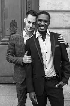 Black and white bw portrait Two boys, caucasian and afro american, wearing suits standing near building and hugging. Concept of gays and lgbt in Paris