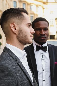 close up portrait of same sex couple. caucasian man wearing suit standing near afro american boy. Concept of business and male fashion.