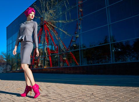 Fashion photo of a beautiful woman in front of a building with reflection of Ferris wheel at summer time